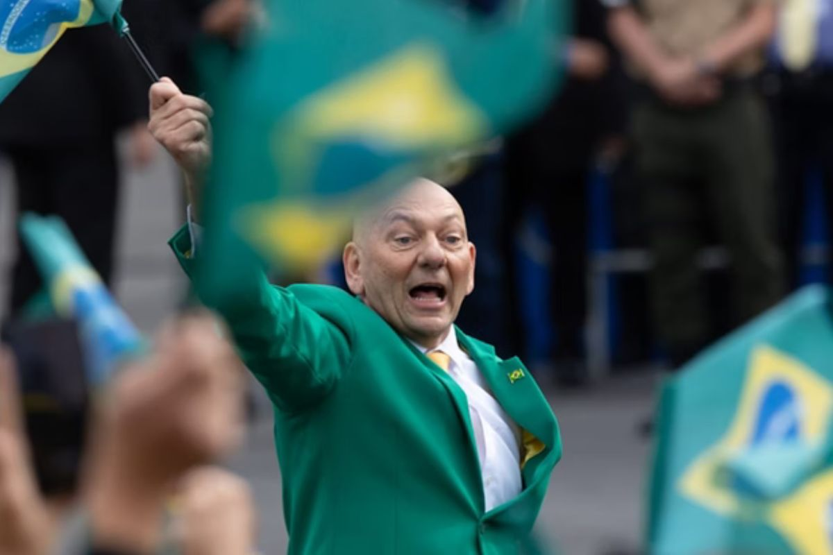 Luciano Hang de roupa social verde, gritando e balançando bandeira do Brasil