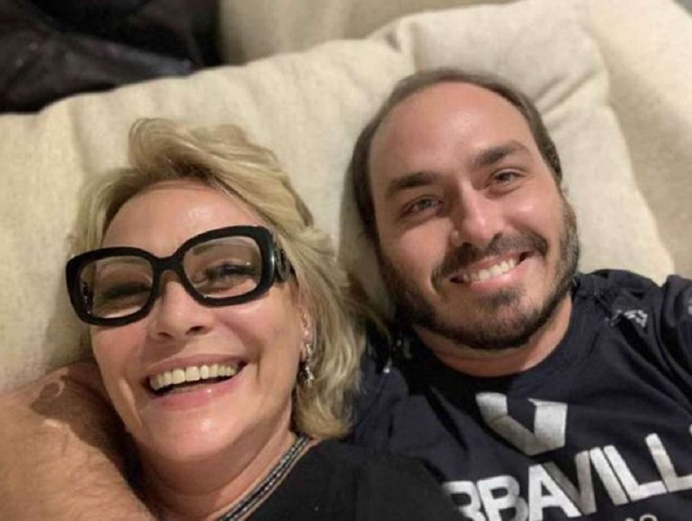 Rogéria Nantes com um dos filhos, Carlos Bolsonaro, ambos deitados e sorrindo