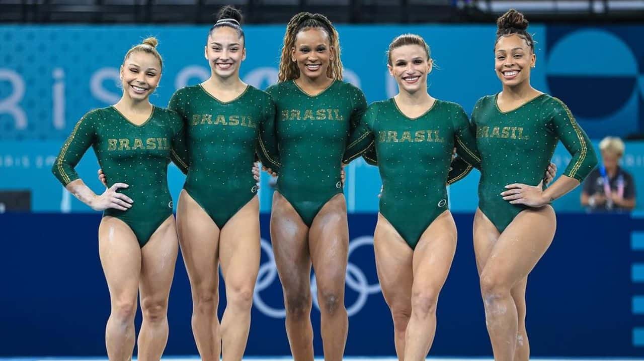 Flávia Saraiva, Julia Soares, Rebeca Andrade, Jade Barbosa e Lorrane Oliveira sorrindo, lado a lado, com uniforme