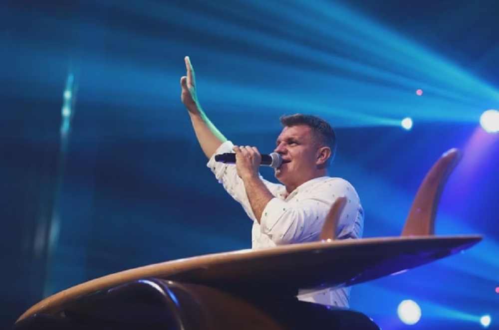 Pastor Rinaldo Pereira, da igreja evangélica Bola de Neve, de perfil, de roupa branca, falando em microfone