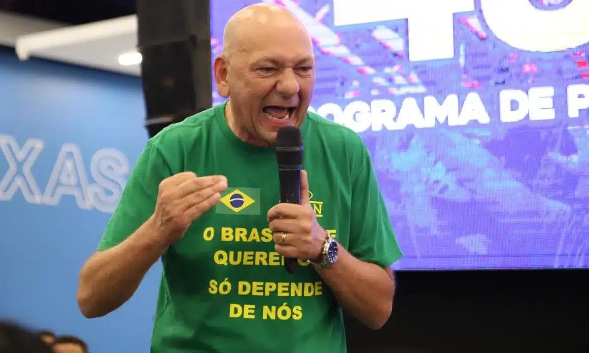 Luciano Hang de camisa verde e amarela, falando em microfone com expressão de raiva