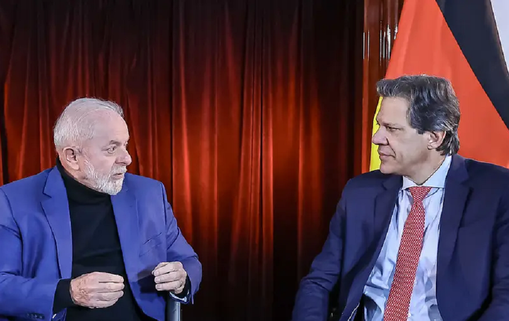 O presidente Luiz Inácio Lula da Silva e o ministro da Fazenda, Fernando Haddad conversando e se olhando, sentados e sérios