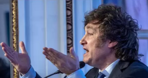 Javier Milei de perfil, falando em microfone e gesticulando, com raiva
