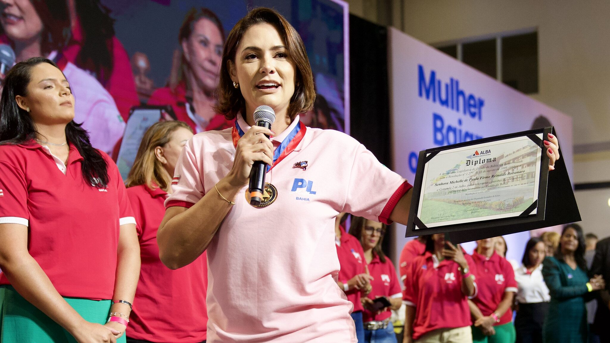 Michelle Bolsonaro de roupa cor de rosa discursando em microfone durante evento