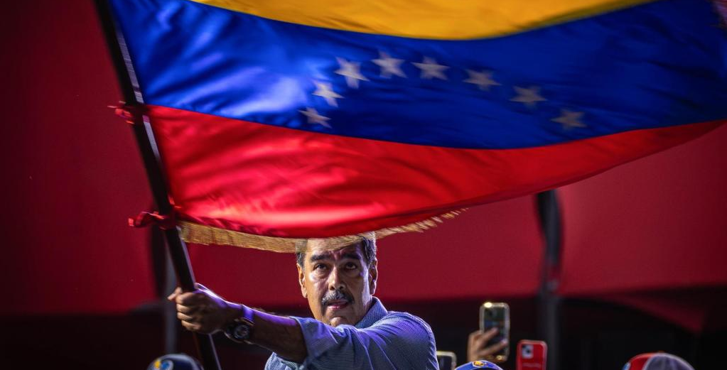 Nicolás Maduro sério, balançando bandeira da Venezuela