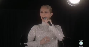 Céline Dion de roupa prata e cabelo preso, cantando em microfone