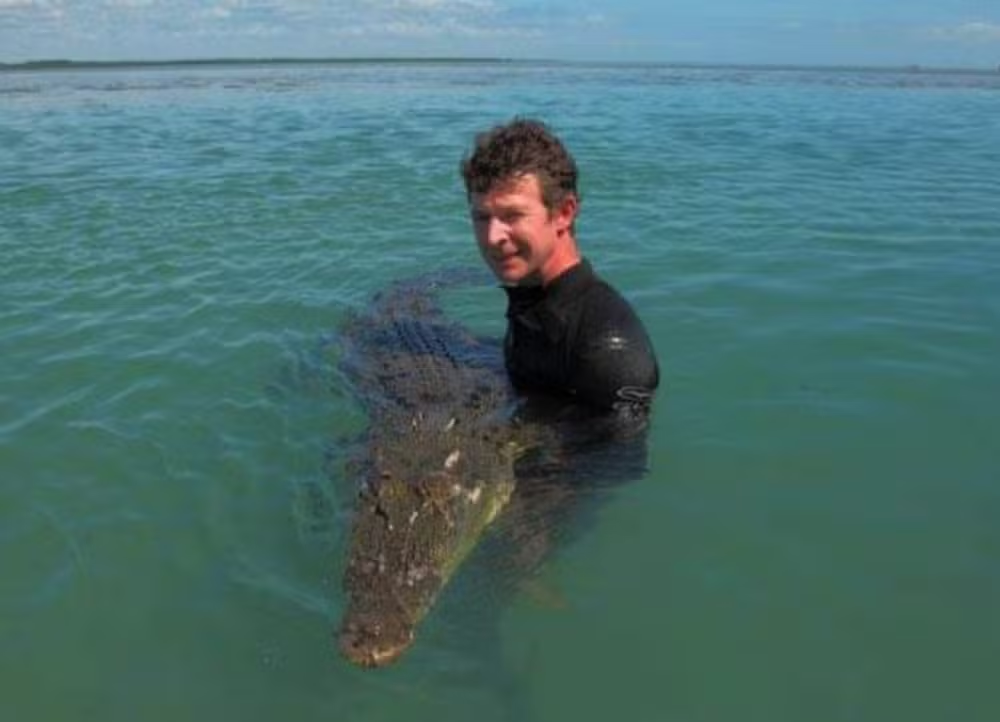 Adam Britton sorrindo para foto na água com crocodilo