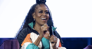 Michelle Obama de roupa colorida, falando em microfone com expressão de celebração