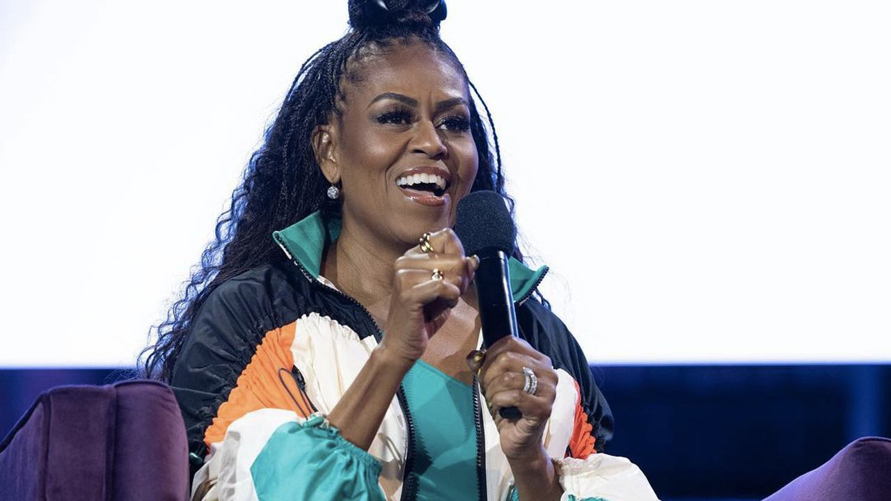 Michelle Obama de roupa colorida, falando em microfone com expressão de celebração