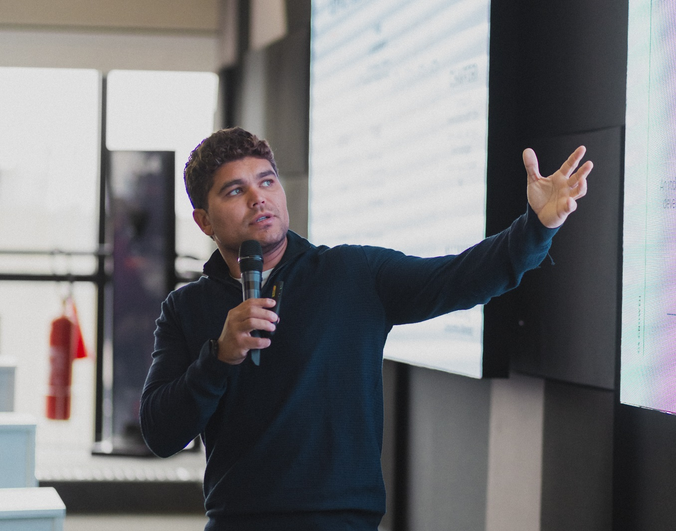 CEO do G4 Educação, Tallis Gomes, de roupa de frio escura, falando em microfone