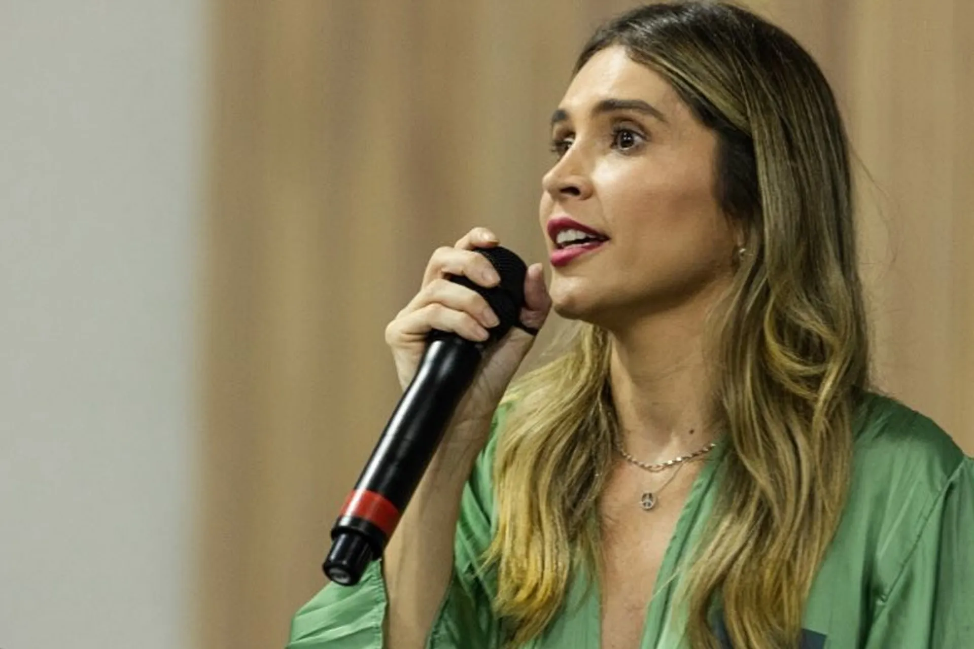 A vereadora Josie Dartora (PV) de perfil, de cabelo solto e roupa verde, falando em microfone