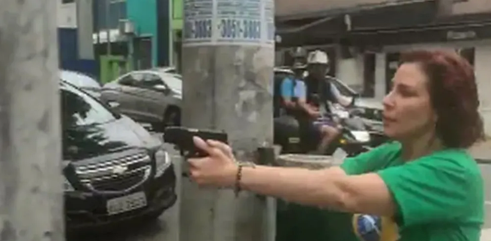 Carla Zambelli de camiseta verde, de perfil, com arma nas mãos, apontando