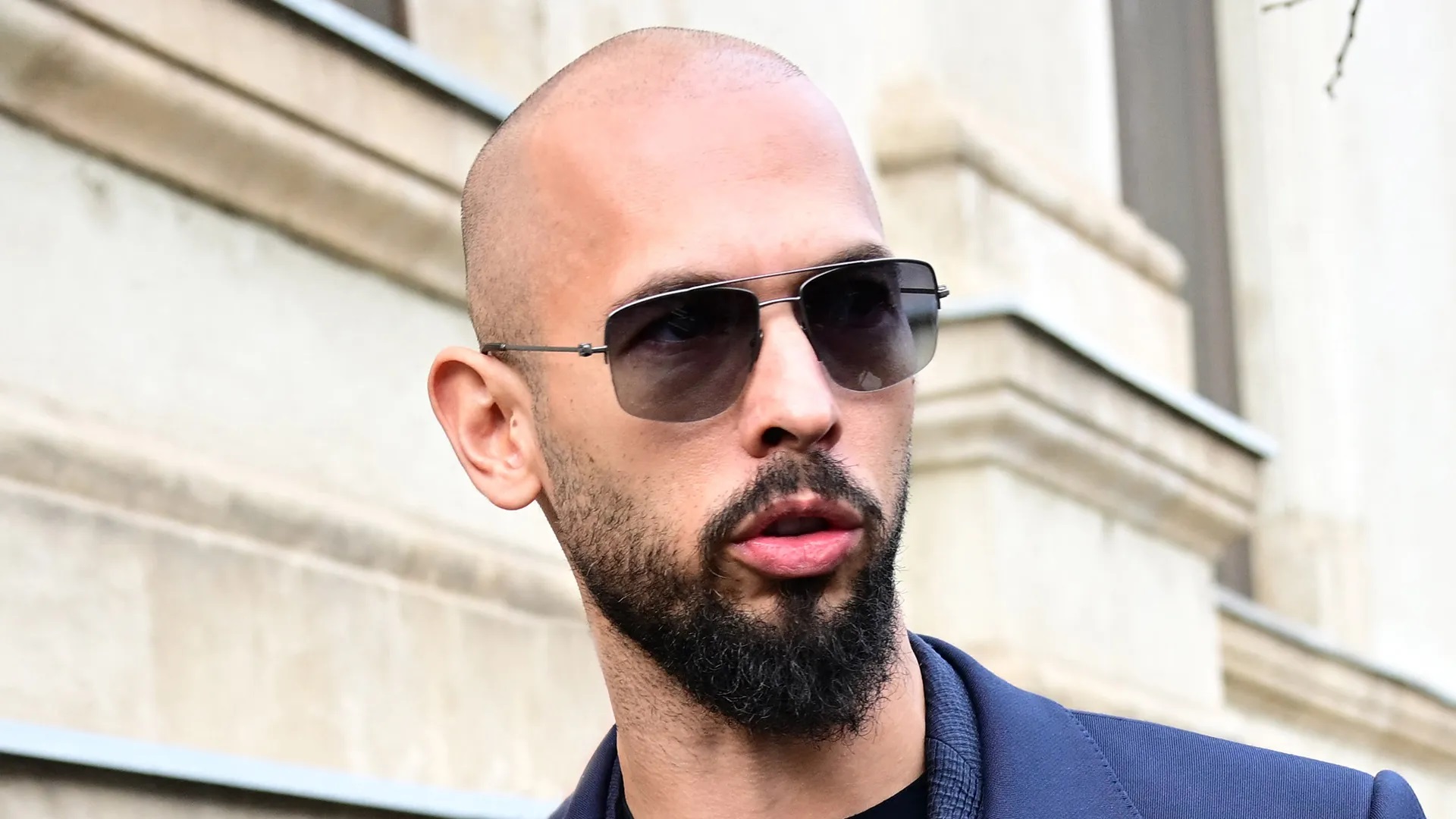 O influenciador britânico-americano polêmico Andrew Tate de óculos escuros, olhando para o lado e falando