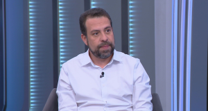 O candidato à Prefeitura de São Paulo, Guilherme Boulos (PSOL) com expressão séria e roupa social clara, sem olhar para a câmera