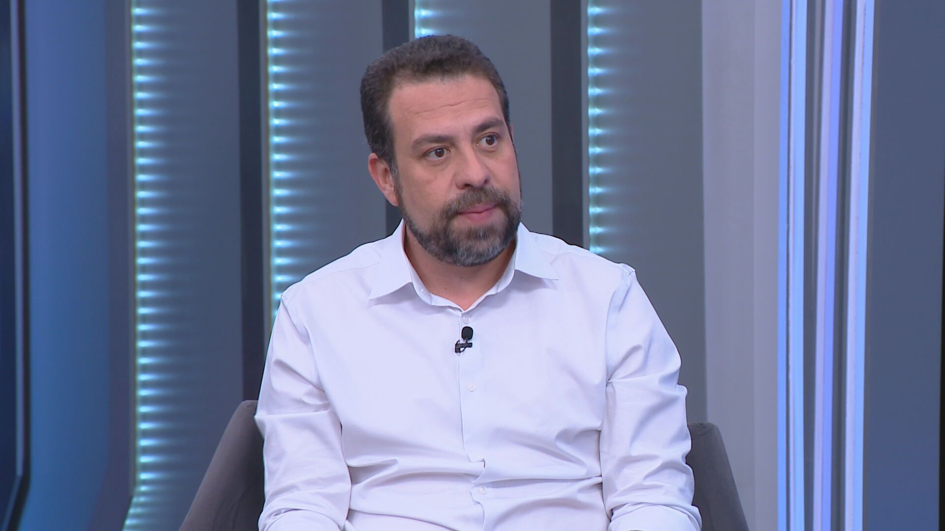 O candidato à Prefeitura de São Paulo, Guilherme Boulos (PSOL) com expressão séria e roupa social clara, sem olhar para a câmera
