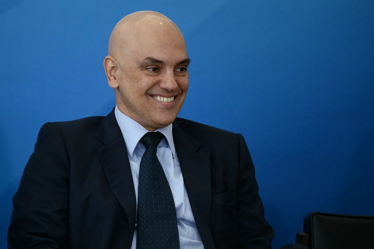 Alexandre de Moraes olhando para o lado e sorrindo, sem olhar pra câmera