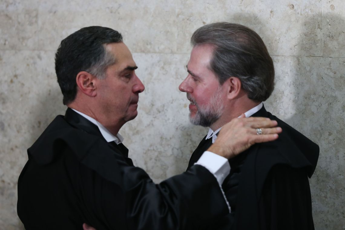 Luís Roberto Barroso e Dias Toffoli de perfil, sérios, se cumprimentando e se olhando, ambos de preto