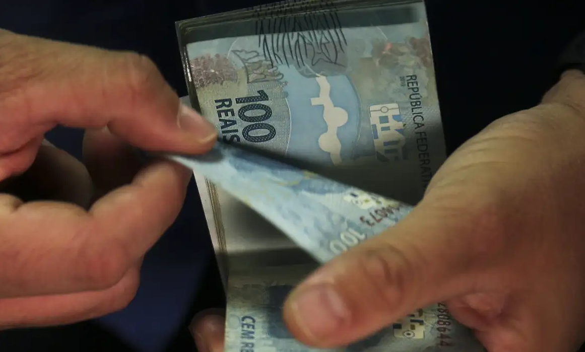 Mãos contando notas de R$ 100