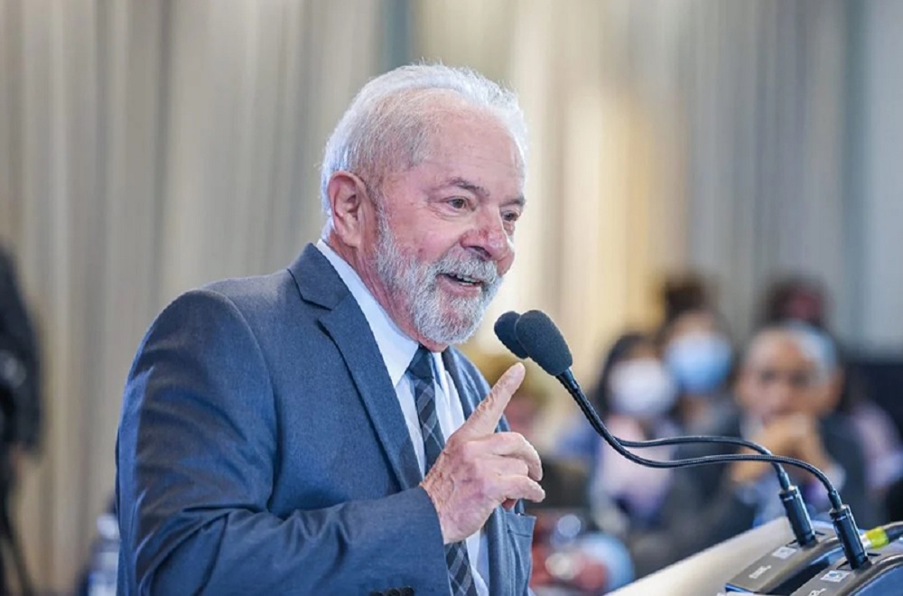 O presidente Luiz Inácio Lula da Silva de perfil, apontando e falando em microfone, sorrindo