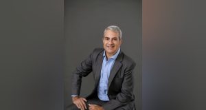 Wilson Pedroso Júnior, também conhecido como Wilsinho, de roupa social cinza, sorrindo, olhando para a câmera, sentado
