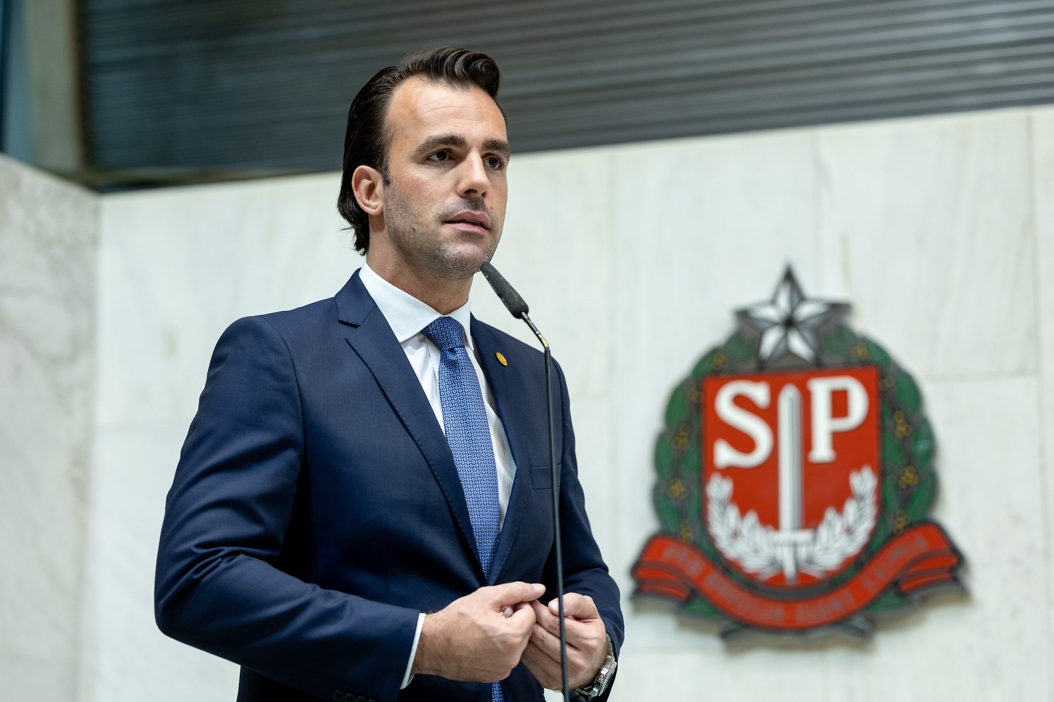 O deputado estadual Lucas Bove (PL-SP) em pé, sério, falando em microfone, sem olhar para a câmera