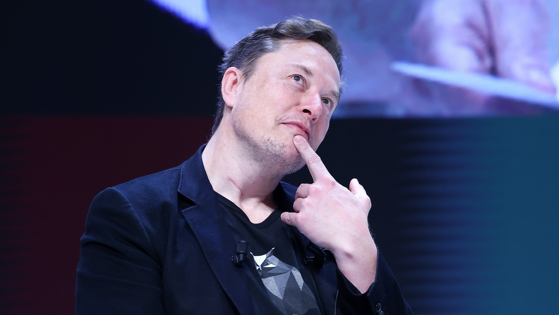 Elon Musk com dedo no queixo, olhando para cima com expressão pensativa