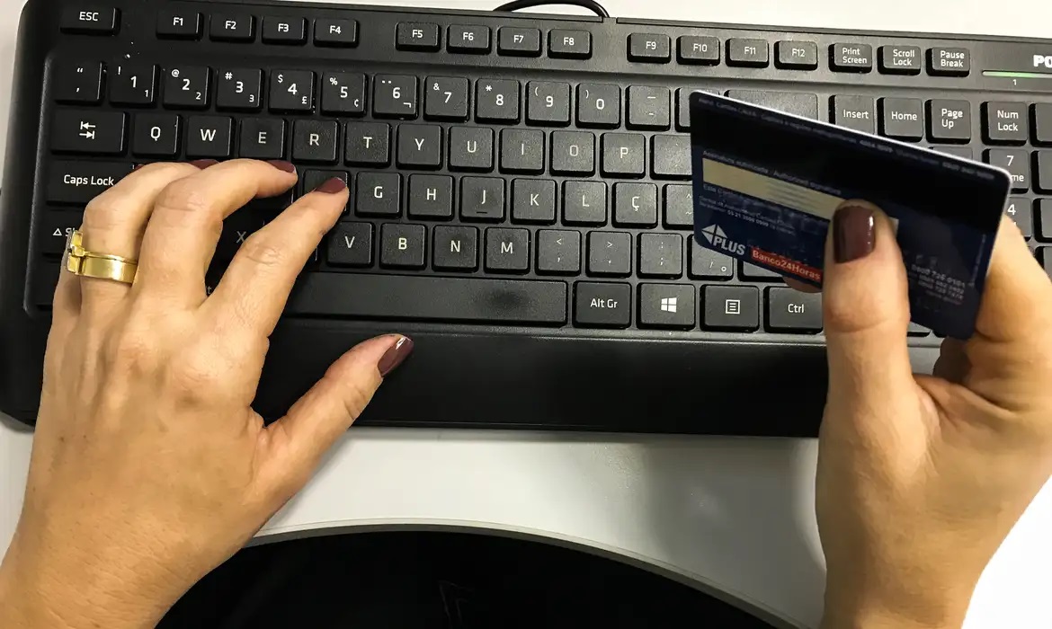 Maos femininas teclando e segurando cartao de banco