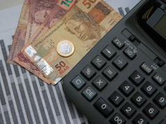Cédulas e moeda de real perto de calculadora