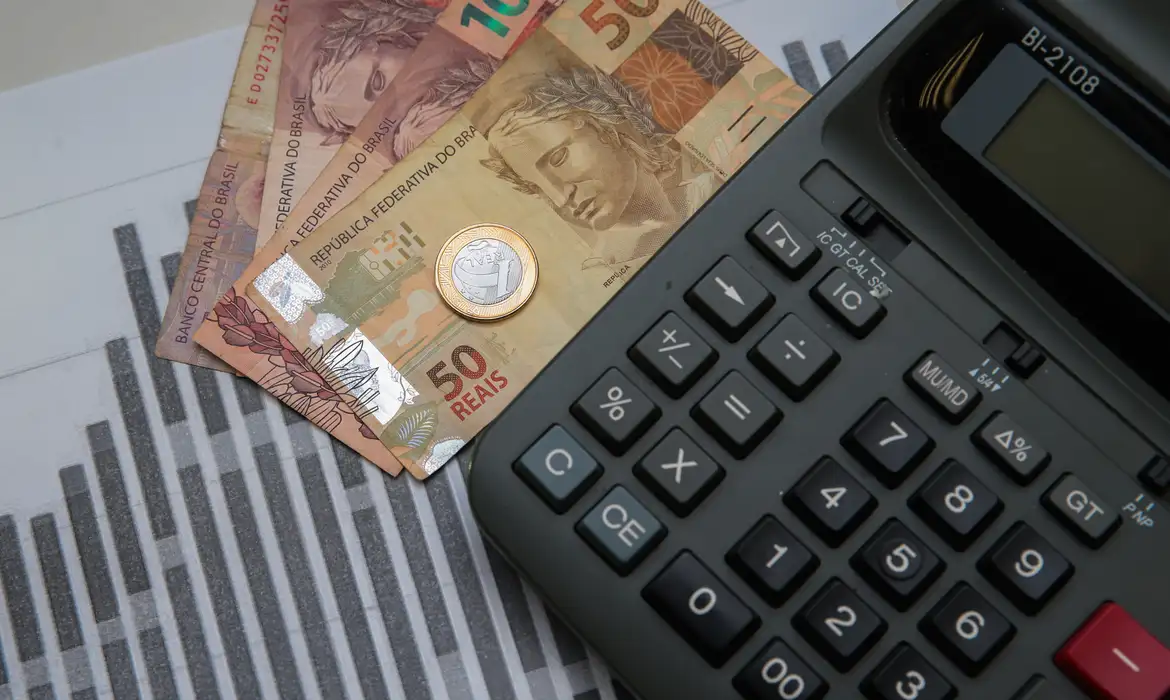 Cédulas e moeda de real perto de calculadora