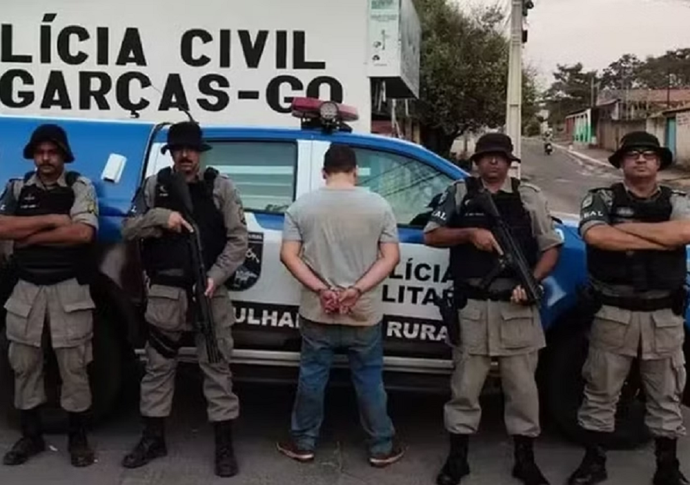 Lucas Vieira de costas e algemado, perto de policiais e carro de polícia
