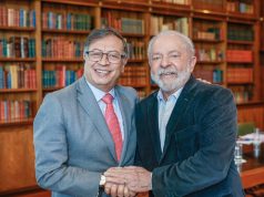 Gustavo Petro e Lula em aperto de mãos, sorrindo e posando para foto com estantes de livros ao fundo