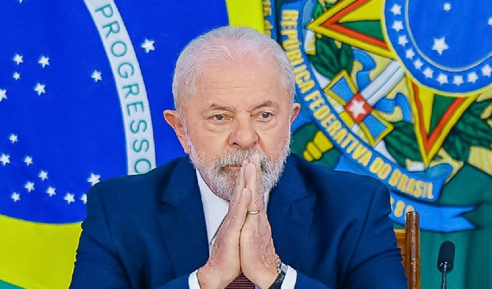 Lula sério, em posição de oração, com bandeiras ao fundo