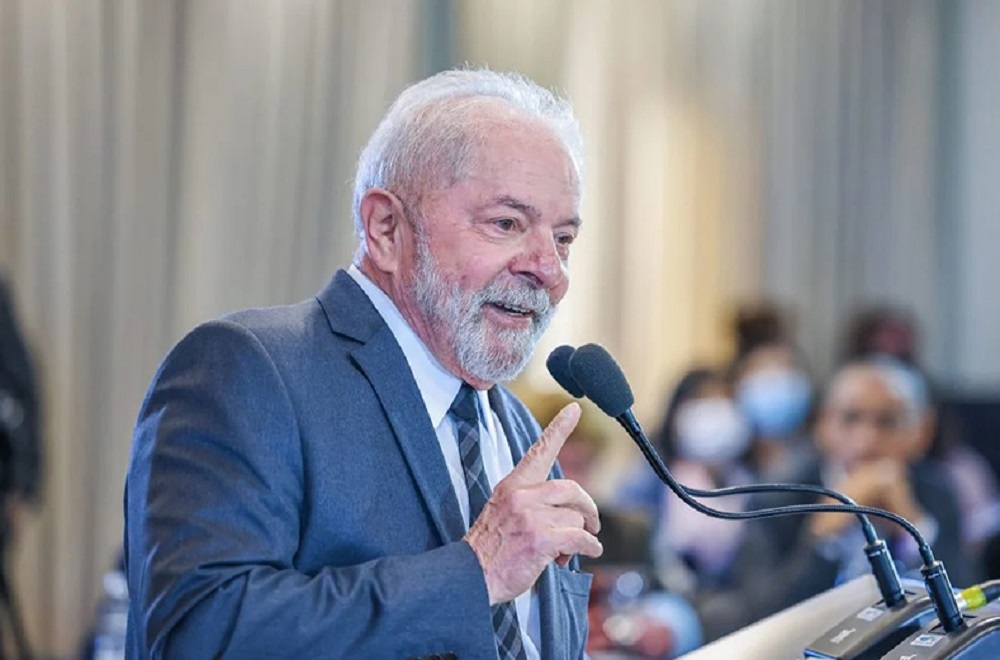 O presidente Luiz Inácio Lula da Silva (PT) de perfil, falando em microfone e sorrindo