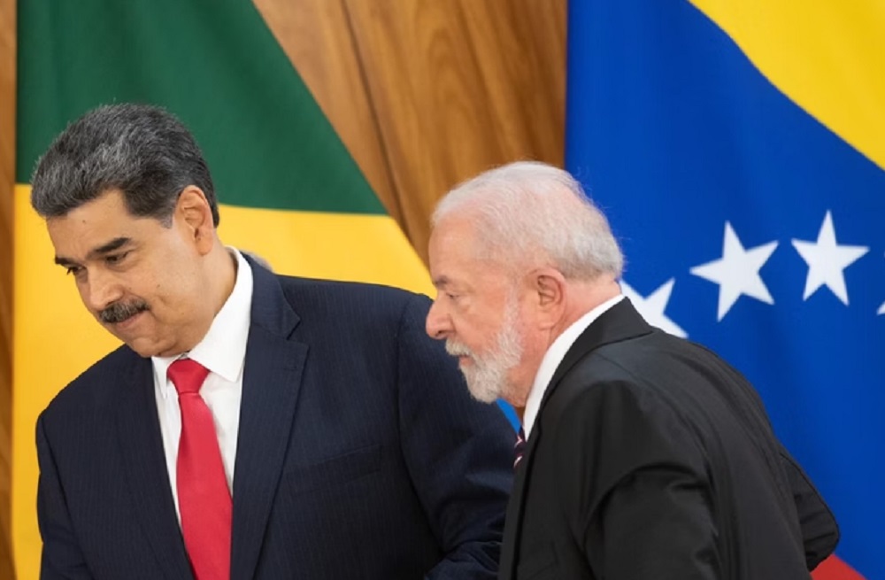 Nicolás Maduro, presidente da Venezuela, e Lula, caminhando, sérios, lado a lado, com bandeiras ao fundo