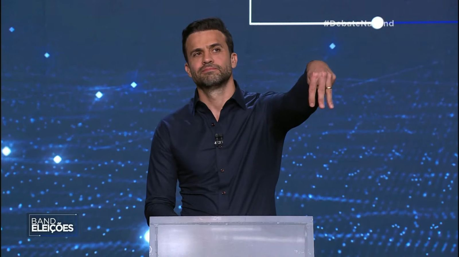 Pablo Marçal (PRTB) de roupa social escura, sério, fazendo o número 3 com os dedos