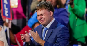 Gus Walz chorando e aplaudindo, com roupa social azul
