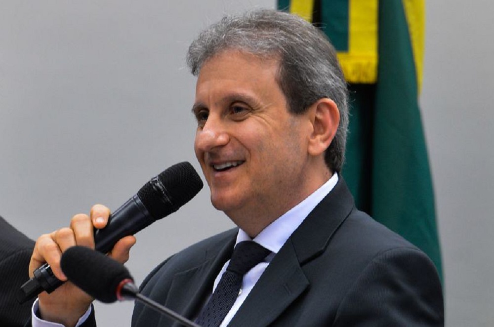 Alberto Youssef de perfil, sorrindo, segurando microfone, de roupa social