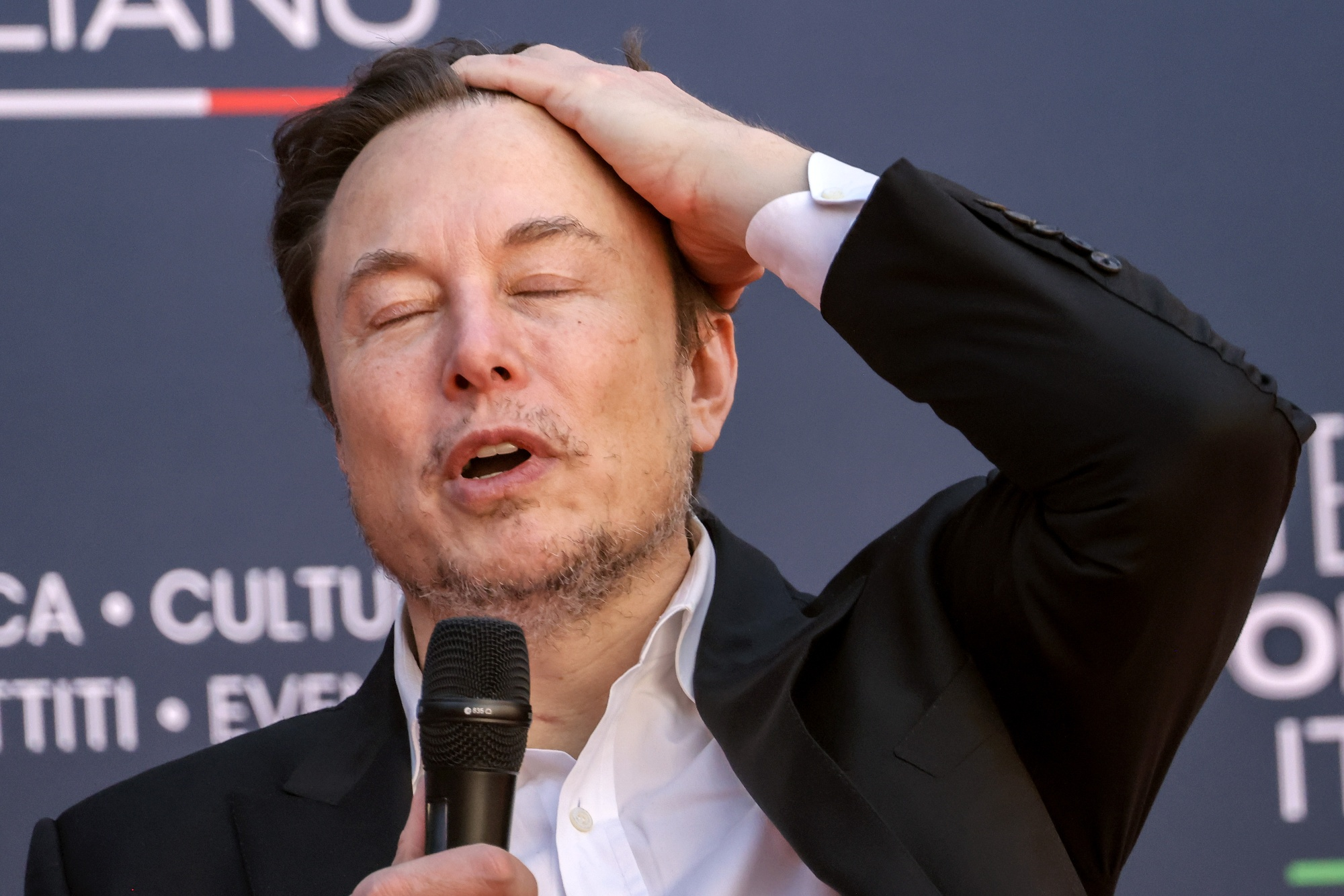 Elon Musk com a mão na cabeça e olhos fechados com expressão de preocupação