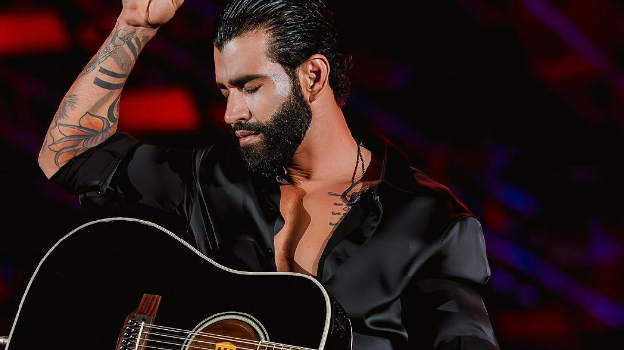 Gusttavo Lima com roupa e violão preto, de olhos fechados em show