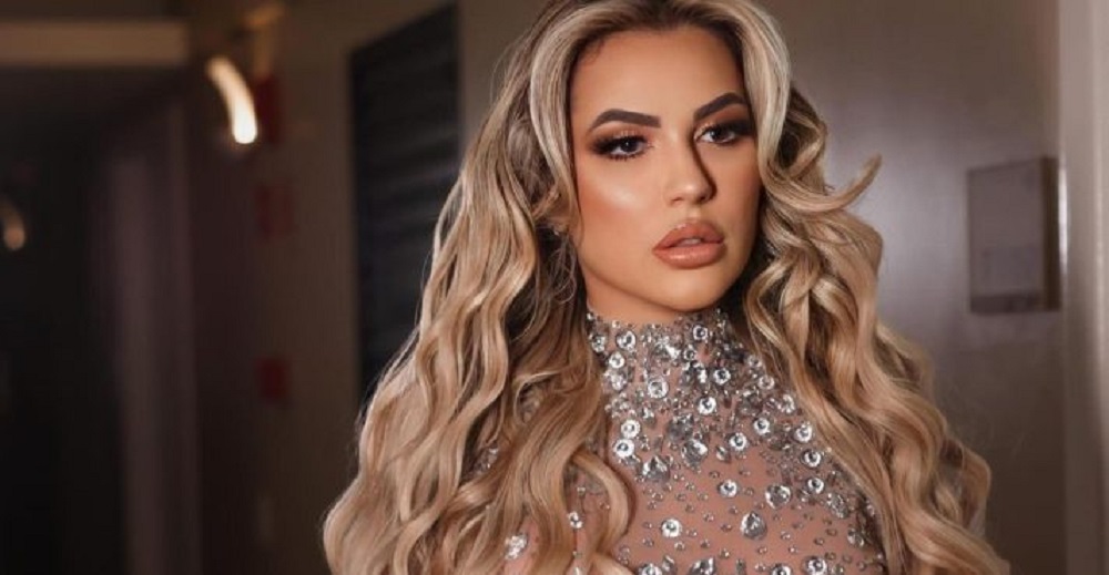 Deolane Bezerra de roupa brilhante e cabelo solto, fazendo carão sem olhar para a câmera