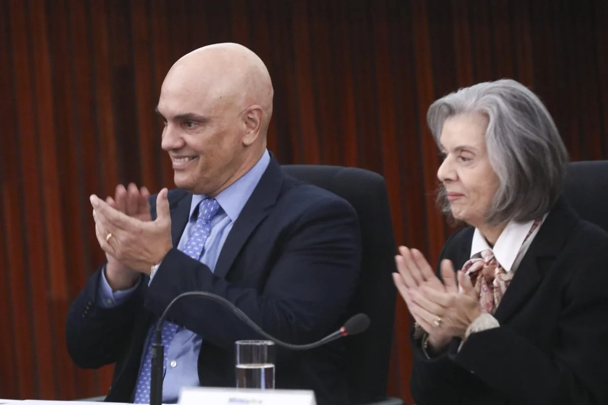 Alexandre de Moraes e Cármen Lúcia de perfil, sorrindo e batendo palmas