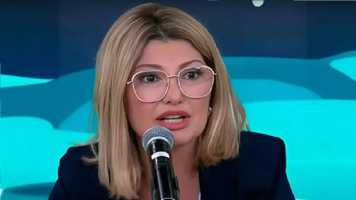 Antonia Fontenelle de roupa escura e óculos, falando em microfone com expressão assustada