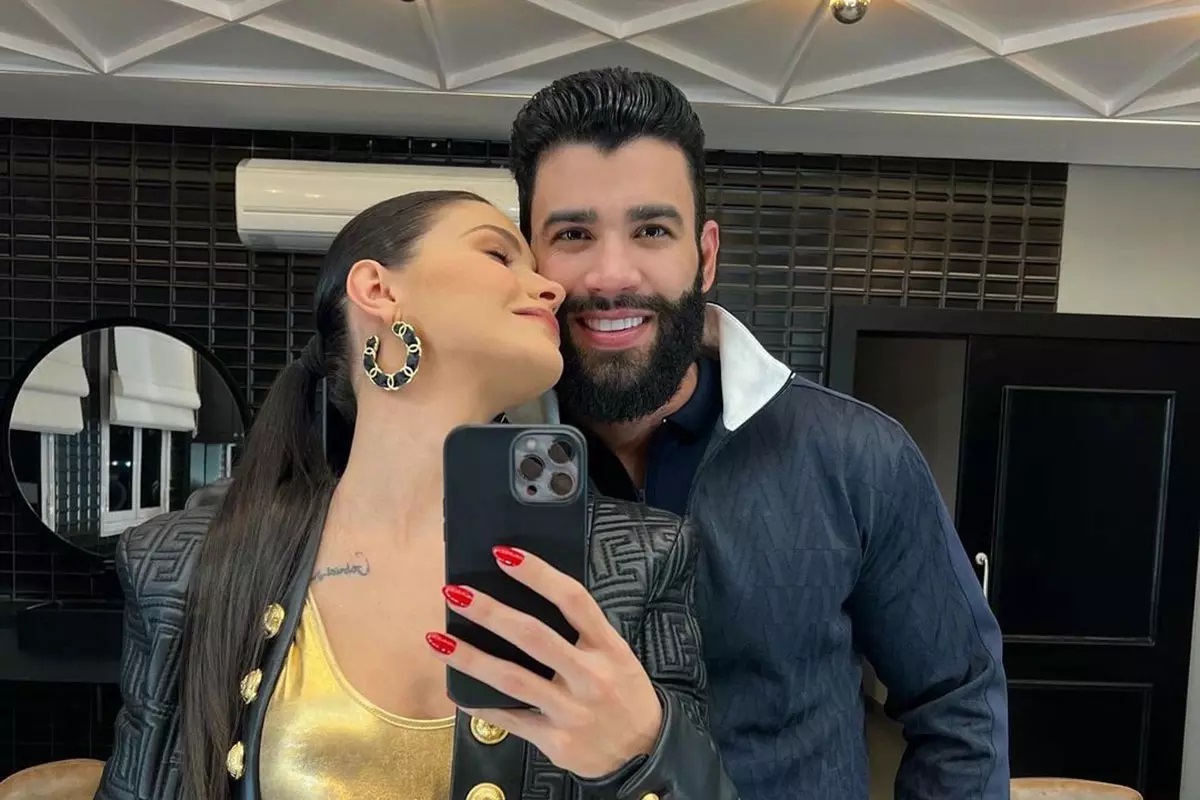 Andressa Suita beijando rosto de Gusttavo Lima enquanto ele sorri para foto no espelho