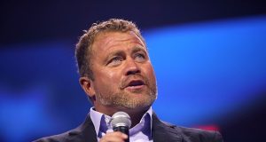 Tim Ballard, ex-agente do Departamento de Segurança Interna, falando em microfone e olhando para cima