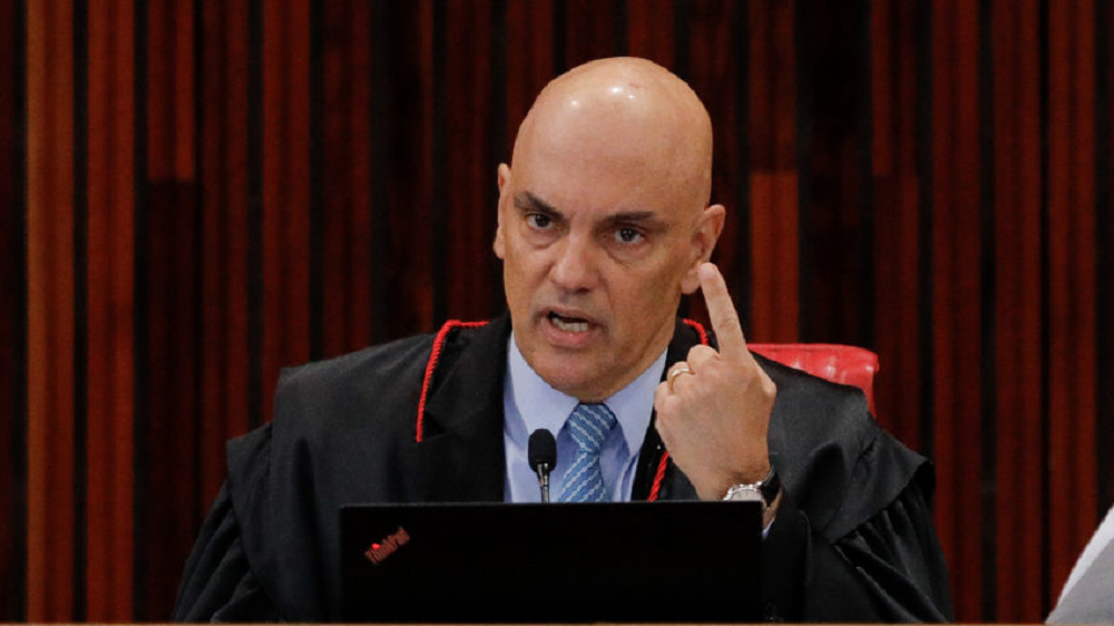O ministro Alexandre de Moraes, apontando pra cima, sério