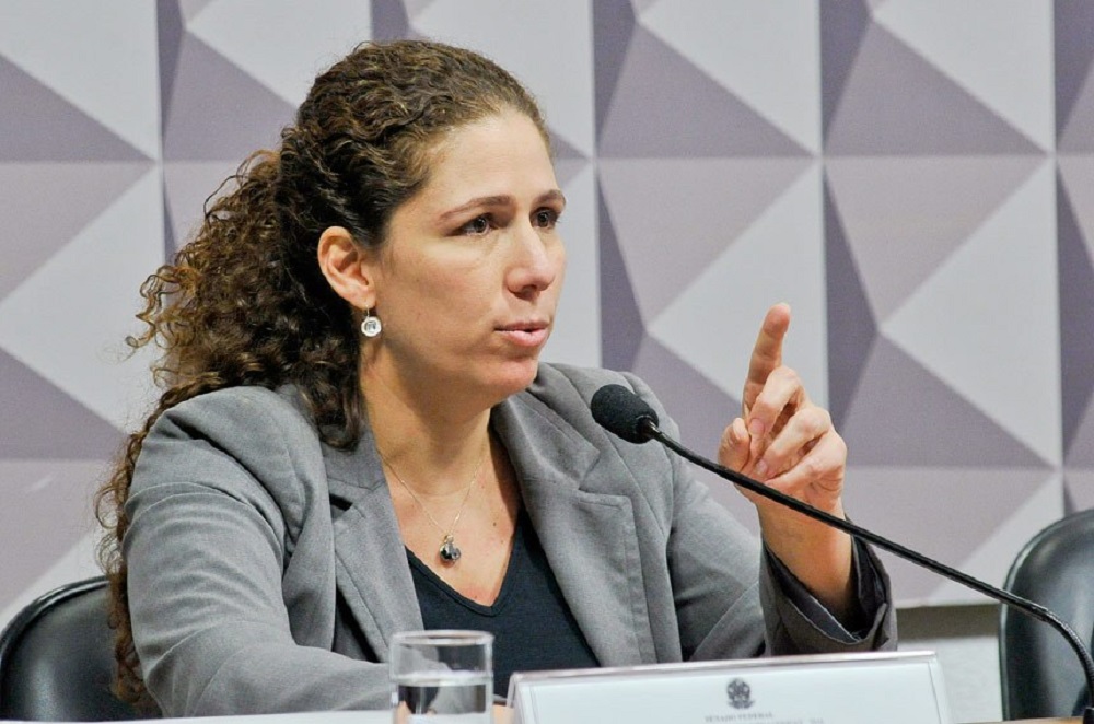 ministra Esther Dweck falando e gesticulando, séria, de roupa cinza