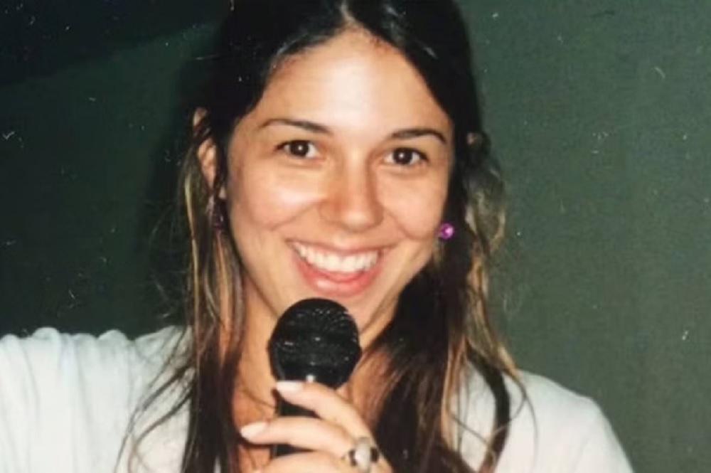 Priscila Belfort sorrindo segurando microfone e olhando para a câmera