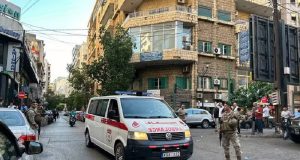 Ambulância no Líbano para socorro de vítimas de explosão de pagers, no meio da rua, perto de pessoas, prédios e outros carros