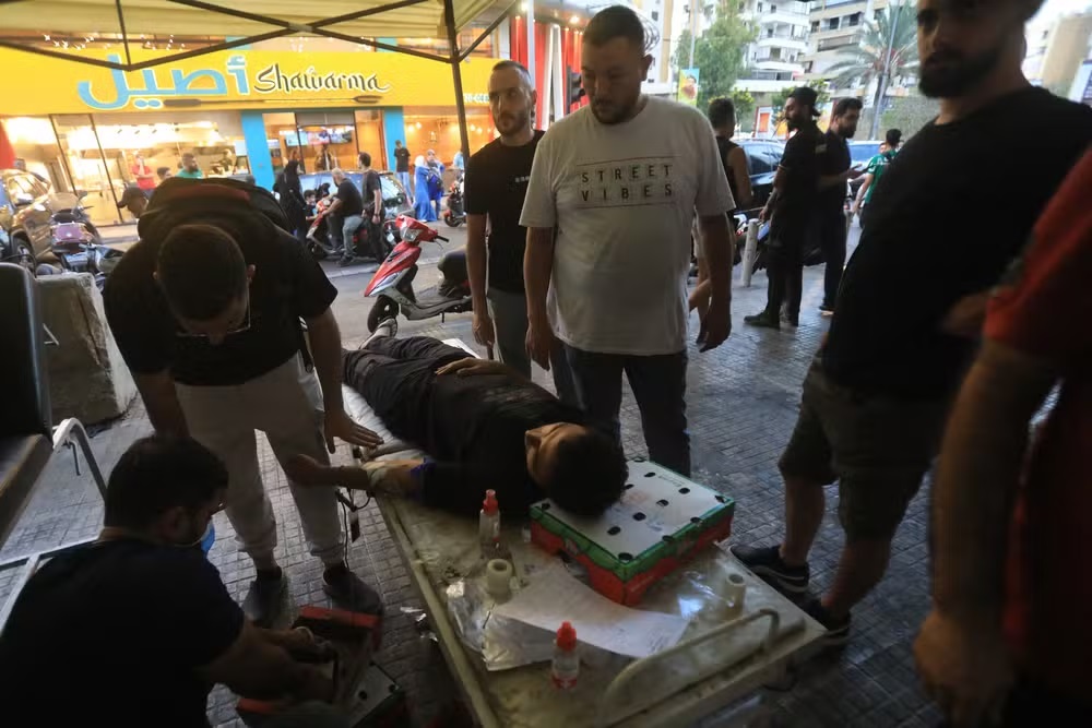 Homem em maca doando sangue, cercado de pessoas, na rua