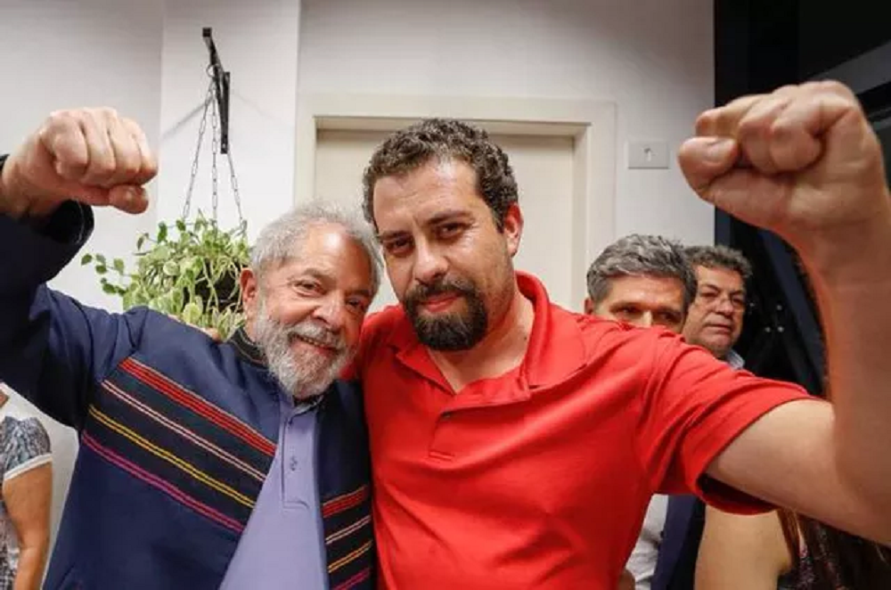 Lula e Boulos posando para foto com sorrisos tímidos e braços levantados